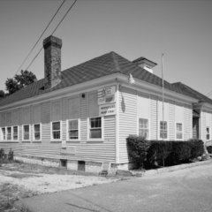 A black and white photo of a well-kept, one-story building with a sign on it announcing “Whitesboro Head Start.” The building is fronted by some ornamental shrubs and a flag pole (no flag). To the left of the photo is a grey box with white letters explaining what the building is.